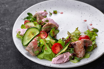 Warm salad with veal and cream cheese, on a white plate and a dark background