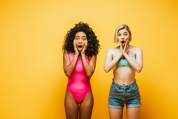 shocked multicultural women in summer outfit touching faces on yellow