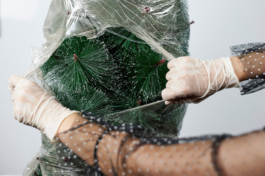 Plastic Wrapped Christmas Tree. Woman In Medical Gloves Cutting And Tearing Saran Wrap. Re-opening Xmas Holidays After Covid-19 Quarantine