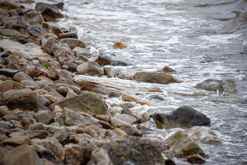 small stones on the seashore, the rolling waves of the sea with foam