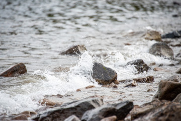 small stones on the seashore, the rolling waves of the sea with foam