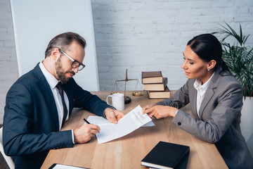 businessman in glasses signing insurance policy contract near lawyer in office