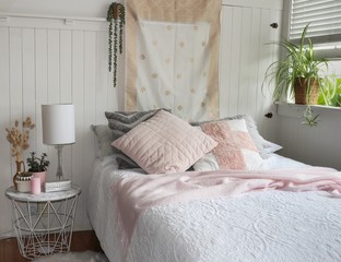 white bedroom with bed and pink cushions and potted house plants
