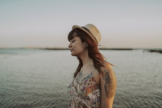 Chica joven y guapa con vestido y sombrero paseando por la playa