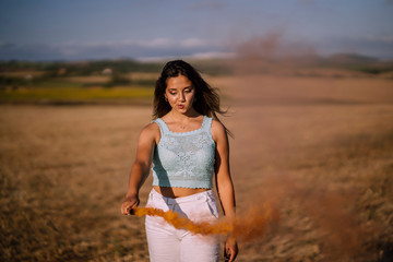 Fototapeta na wymiar Chica joven y guapa por un campo con una bengala de humo 