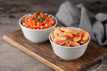 Boiled shrimp prawns in a shell  in a bowl and tomatoes on a wooden background. Top view