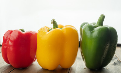 red, green and yellow sweet bell peppers on wood background, paprika, organic vegetables
