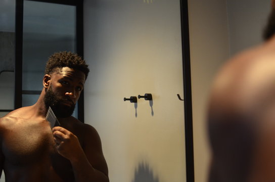 Handsome African American man grooms his beard in the mirror