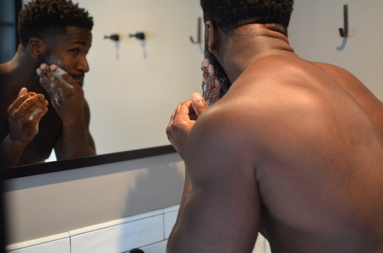 Handsome African American man grooms his beard in the mirror