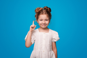 Ginger girl pointing up with forefinger wearing a white dress on a blue studio wall