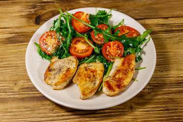 Fried chicken breast with salad of fresh arugula and cherry tomatoes on wooden table