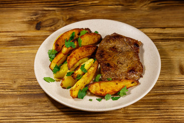 Fried beef steak with potato wedges on wooden table
