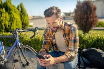 Satisfied man with smartphone sitting near bike