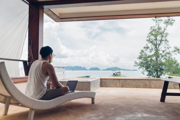 Asian man relax on the bench and working on his laptop with sea view.