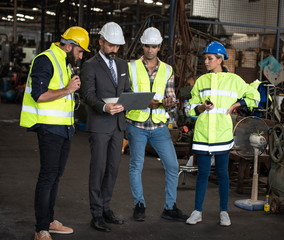 Group of factory workers consists of Manager, Engineers, Technicians with hardhat and vest jacket, discussing about industrial factory production management  by using computer notebook for information