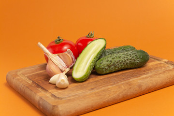 Sliced cucumber, tomatoes and garlic on wooden cutting board. Tomatoes with green ponytails. Healthy food. Copy space. High quality close-up photo