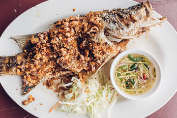 Thai deep fried fish with garlics and spicy sauce served on white dish.