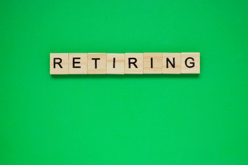 Word retiring. Wooden blocks with lettering on top of green background. Top view of wooden blocks...
