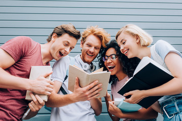low angle view of excited multicultural students reading book on urban street