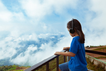Fototapeta na wymiar Asian child girl listening the music with headphone and looking at the beautiful mist and mountain with freshness and happiness