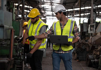 Two industrial Engineers and Technician workers with helmet or hardhat working and checking machinery on notebook or laptop in industry manufacturing Factory