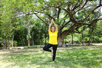 Smiling Asian young woman in yellow sportwear standing and doing yoga for meditation for create concentration and calm the mind on grass field after exercise in the natural light garden.