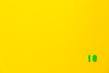 A green plastic toy number eighteen is located in the lower right corner on a yellow background