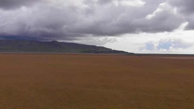Aerial footage of the Eyjafjallajökull volcano mountain range from a beautiful green and yellow meadow with cloudy sky. Seljalandsfoss waterfall in the background.