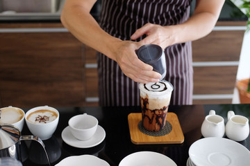 Asian barista young man pouring fresh Chocolate art in a plastic glass of Cappuccino iced coffee for according to order at counter bar in the morning at modern cafe.