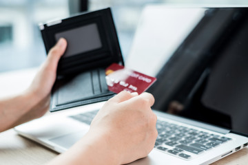 The businesswoman's hand is holding a credit card and using a laptop for online shopping and internet payment in the office