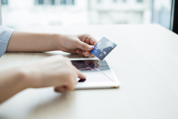 The businesswoman's hand is holding a credit card and using a laptop for online shopping and internet payment in the office