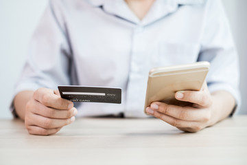 The businesswoman's hand is holding a credit card and using a smartphone for online shopping and internet payment in the office