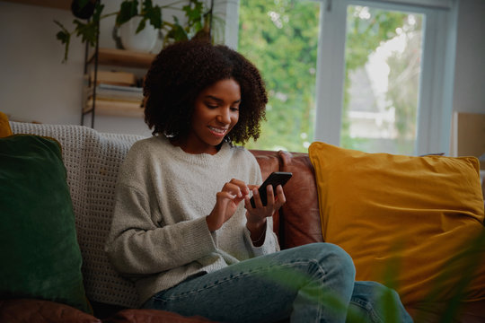 Smiling girl relaxing at home using cellphone for texting and chatting with friends