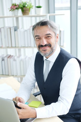 Smiling Smart Caucasian senior manager and businessman in black suit relaxing in social media online and talking, calling with businesspeople on smartphone at workspace in office