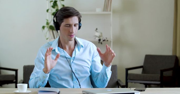 Happy businessman relaxing in office at desk listening music in wireless headphones, moving arms as if playing drums, singing. Funny male wearing shirt feel bored, dance cheerful to relax, hard work