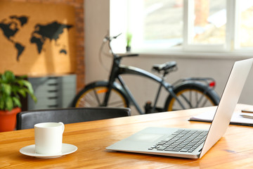 Laptop and cup of coffee at workplace in modern office