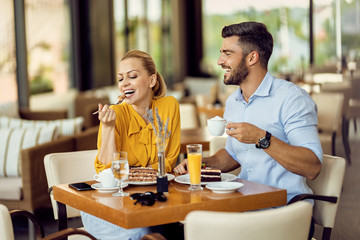 Happy couple having fun while eating cake and drinking coffee in a cafe.