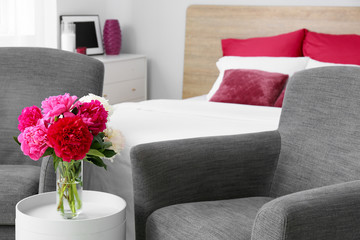Interior of modern stylish bedroom with armchair and bouquet of flowers on table