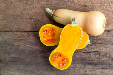 Butternut squash whole and sliced ​​on a wooden table. Butternut is a bell-shape fruit with...