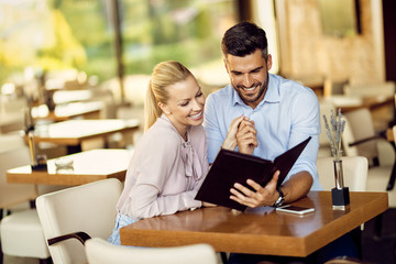 Happy couple holding hands while choosing an order from a menu.