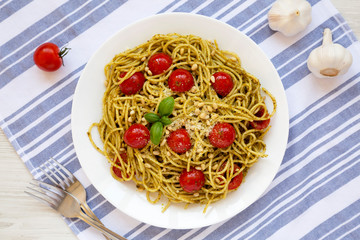 Homemade Pesto Pasta with Tomatoes and Pine Nuts on a white plate, overhead view. Flat lay, top view, from above.