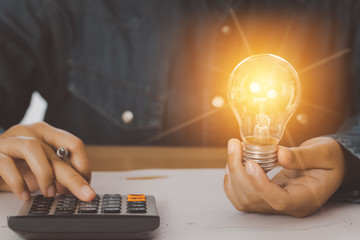 Human hand holds a light bulb and presses a calculator to calculate the company energy use numbers....
