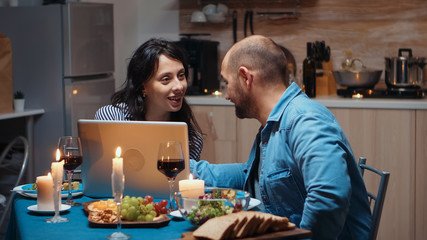 Excited caucasian lover couple dining together and using laptop. Adults sitting at the table, searching, browsing, surfing, using technology, enjoying the meal in the dining room