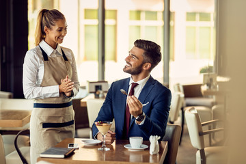 Young happy waitress talking to a businessman in a cafe,
