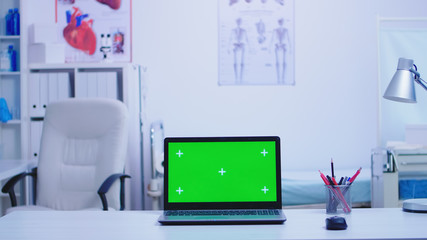 Laptop in hospital cabinet with green screen and nurse wearing blue uniform holding protection mask. Notebook with replaceable screen in medic clinic.