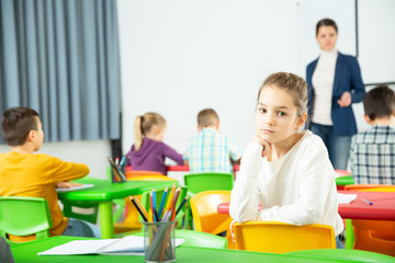 Sad bored schoolgirl sitting separately in classroom during lesson in elementary school