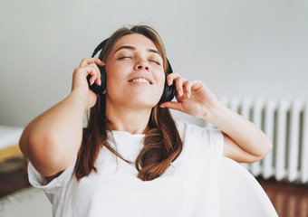 Portrait of smiling young woman brown hair and green eyes with freckles in the white t-shirt and jeans listening music by headphones