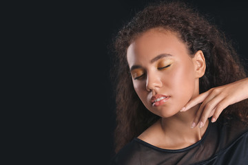 Young African-American woman with beautiful eyeshadows on dark background