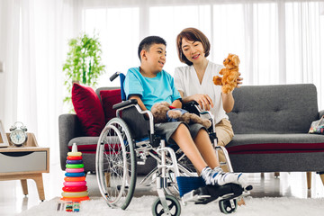 Portrait of enjoy happy love family asian mother playing and carer helping look at disabled son child sitting in wheelchair moments good time at home.disability care concept