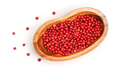 Red or Pink peppercorn in small wooden bowl, some scattered on board near, closeup photo isolated with white background